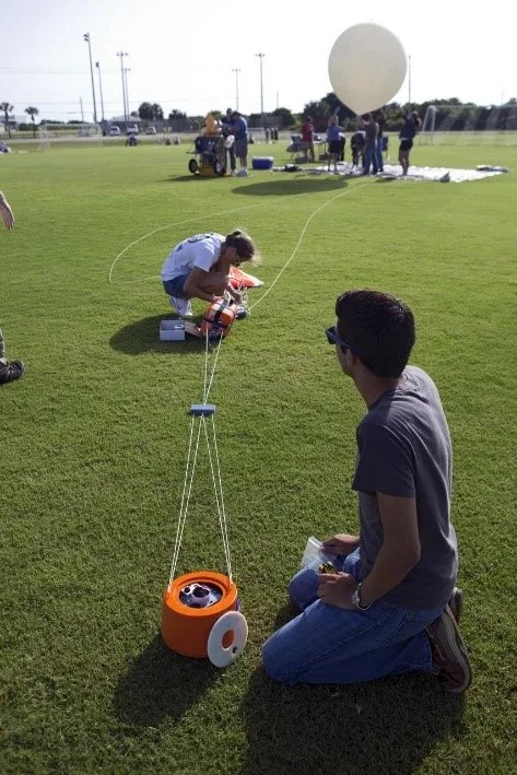 Two students in a field preparing a white balloon for launch