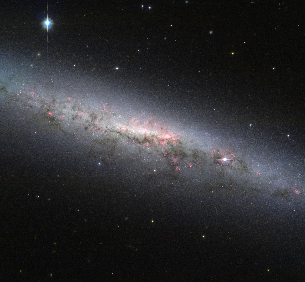 A pale milky galaxy seen on edge - with pink clusters of star-forming regions sprinkled through the center