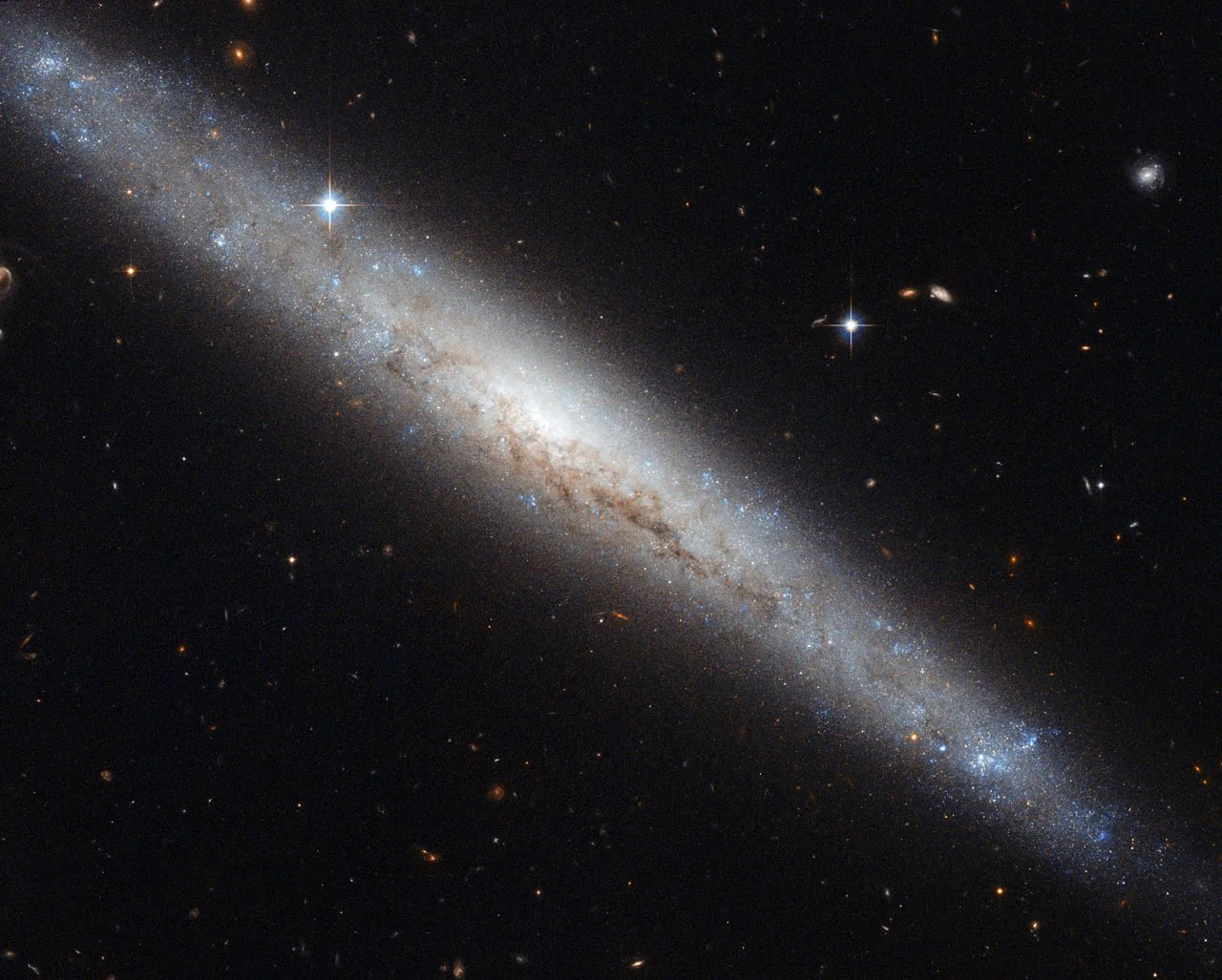 A fuzzy, edge-on spiral galaxy bend sinister with dust lanes lacing the thickest part
