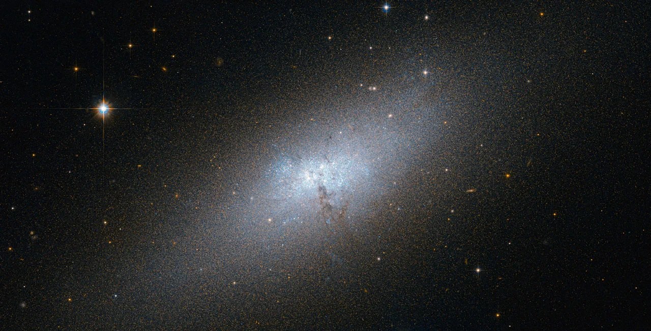 diffuse fuzzy blue galaxy with no spirals but clouds of brighter and darker material near the center