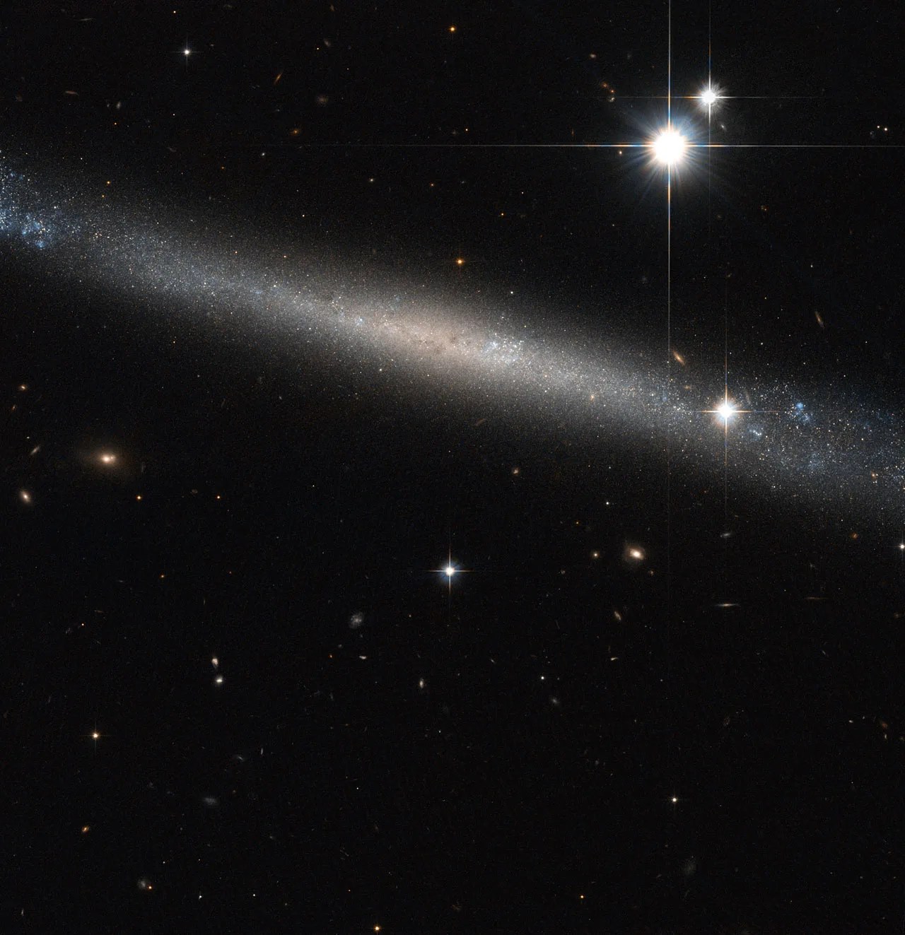 a thin sliver of a galaxy seen edge on - one of the flattest Hubble has imaged - with two bright stars burning upper right