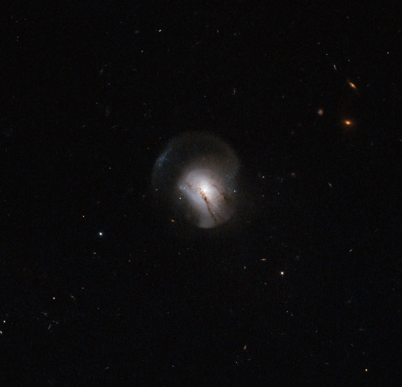 A distant bubble of light, streaked with threads of dust and encircled by an outer bubble amid a spare field of distant pinpoints and tiny galaxies.