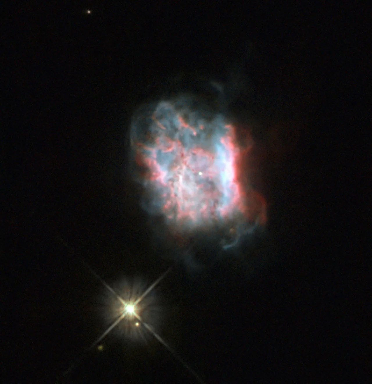 A bright yellow starburst next to a bright, burst star - pink and white tendrils of gas dissipate away from a central glowing disc