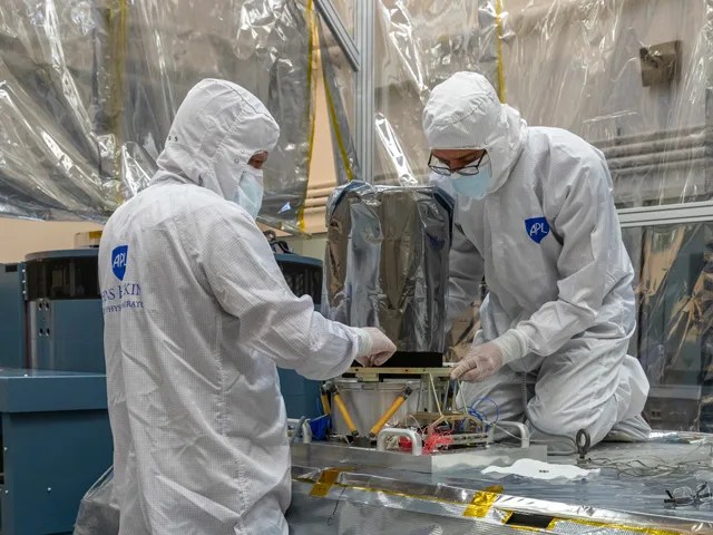 two people in protective suits work on a foil-covered instrument box