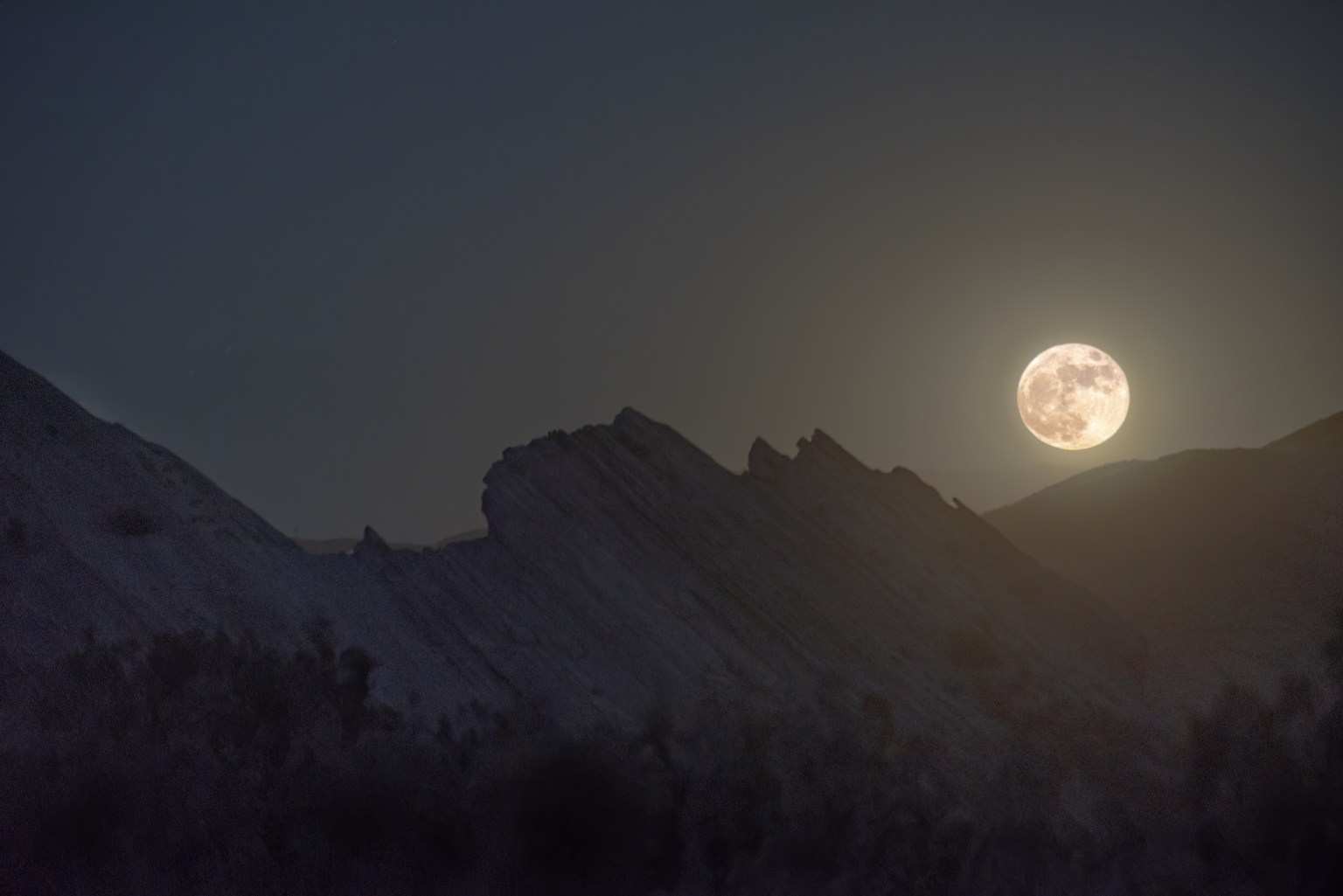 The Moon rises above a jumbled collection of giant rocks.
