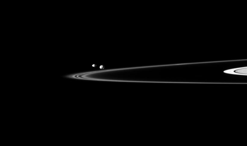 Two of Saturn's small moons can be seen orbiting beyond the planet's thin F ring