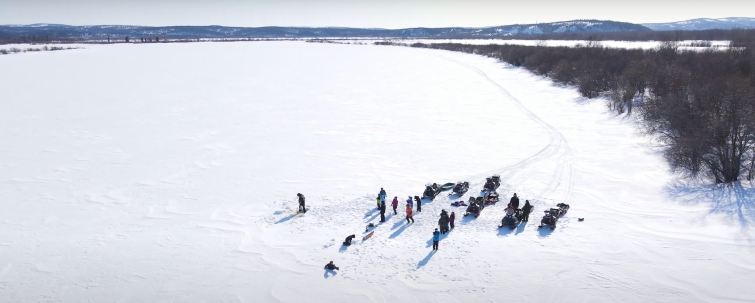 Aerial photograph of about 20 people in colorful jackets gathered on the ice